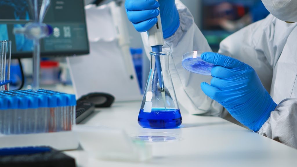 close up science technician ppe suit using pipette with microtiter plate petri dish working laboratory team examining virus evolution vaccine development against covid19 1024x576 1